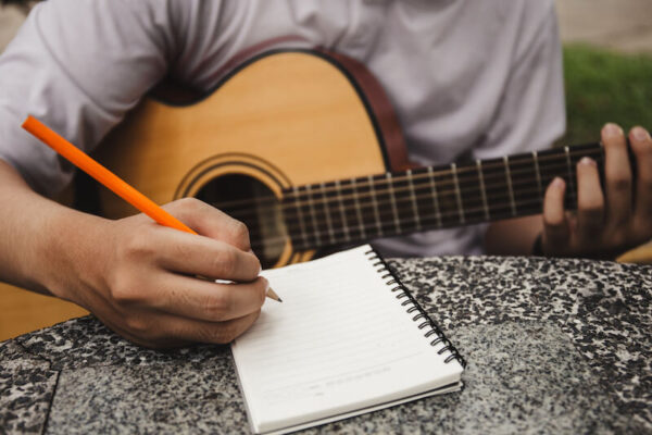 Man sitting with guitar and writing lyrics on a notepad