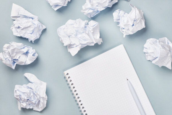 Notebook and pen surrounded by crumpled paper balls
