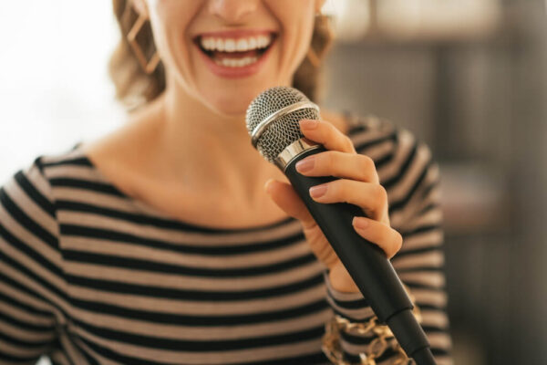 Woman wearing a striped shirt holding microphone in hand and singing into it