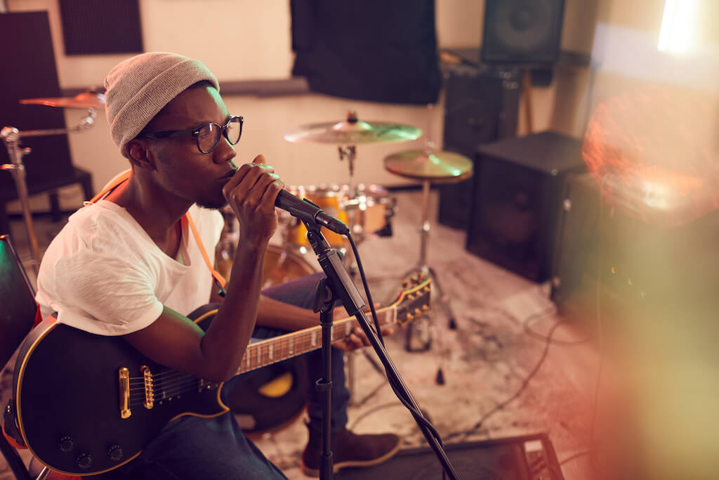 Male musician sitting while holding a guitar and singing into a microphone