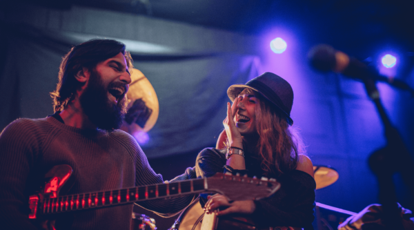 One man on the left playing guitar next to a woman singing at a live show