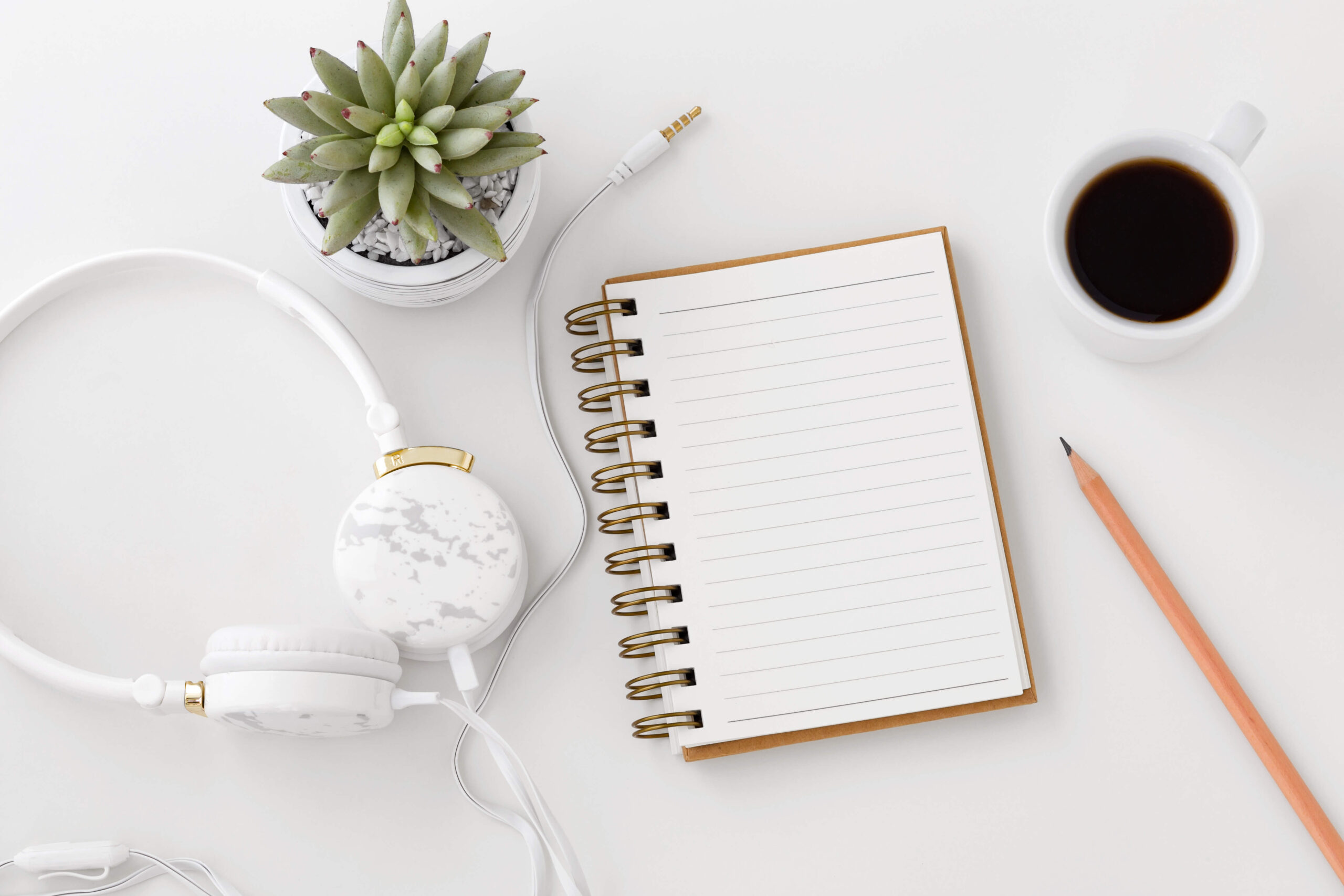 White surface with blank open notebook a pencil coffee and earphones spread around it