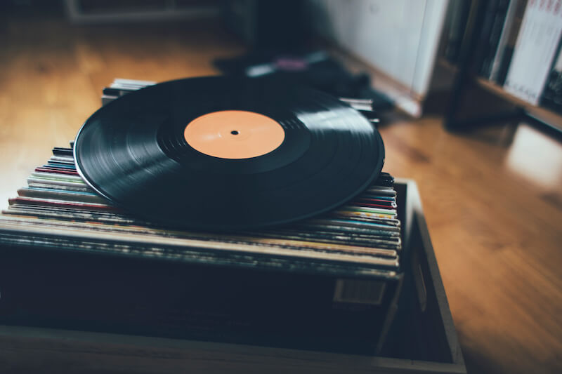 Image of record sitting on top of a box of records with wood flooring below it