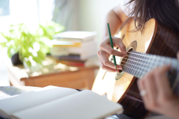 Girl holding a guitar while writing music looking at down at her notebook
