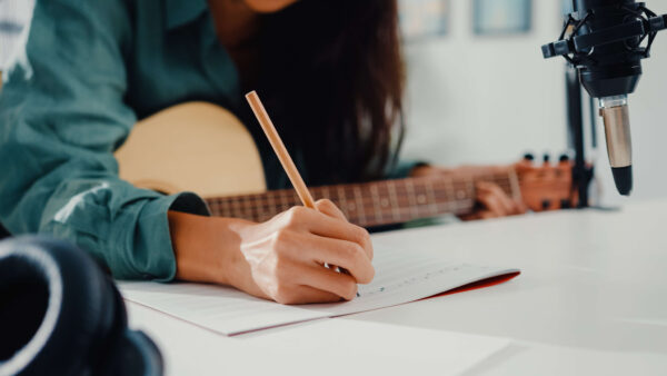 Girl holding a guitar and writing music with a pencil
