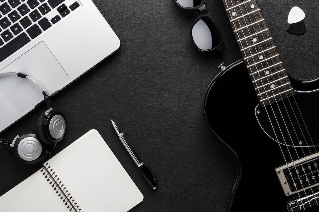 Black and white image with laptop keyboard and journal on the left and guitar on the right. 
