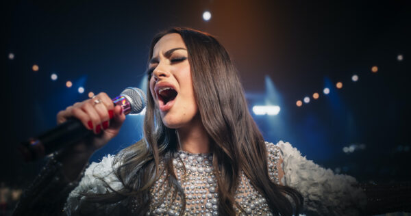 Close Up Portrait of a Pop Band Lead Singer Performing a Hit Song on Stage, Inspiring a Large Audience of Music Enthusiasts. Brunette Female Musician Performing a Concert in a Stylish Pearl Outfit