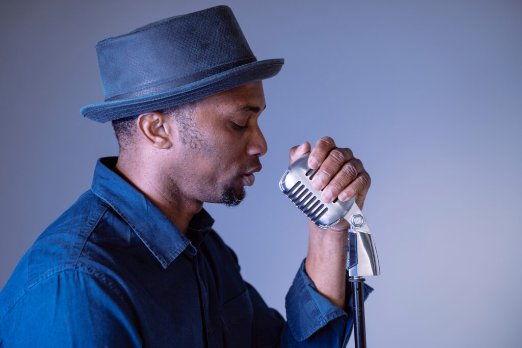 a hipster man singing a vintage song. Isolated male performing ethnic cultural songs. Young african american singer holding trendy microphone. Compose and create lyrics.